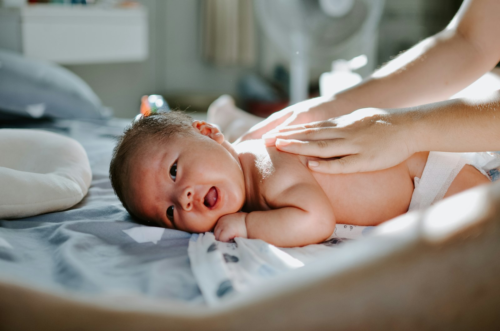 Blähungen beim Baby: Mutter massiert sanft den Rücken ihres Säuglings auf dem Bett