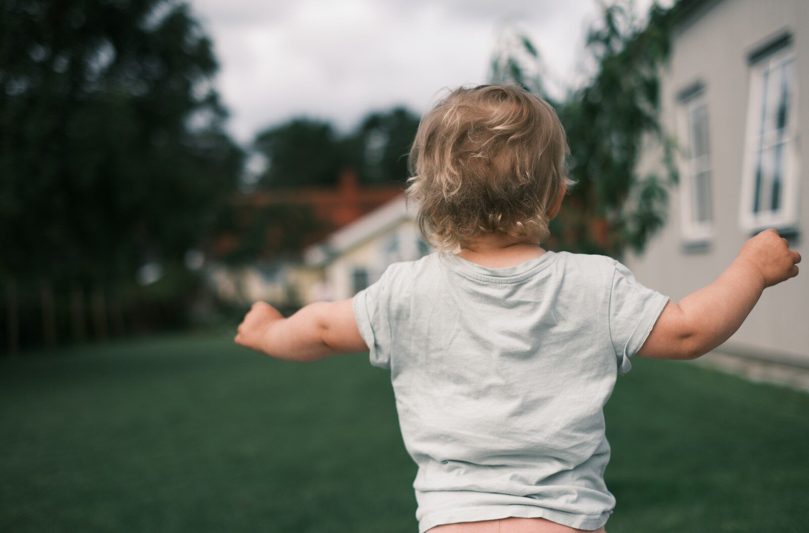 A little boy standing in the grass with his arms outstretched